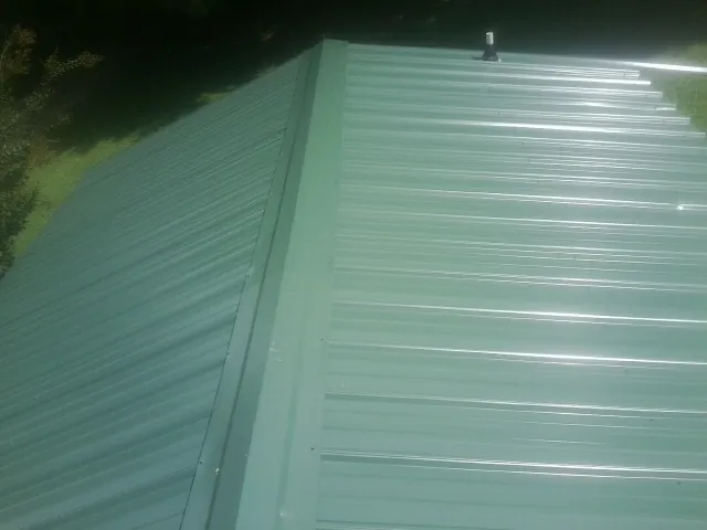 New green metal panels meeting at the ridge of a roof — Flat Roof Repair work by our crew in Onalaska